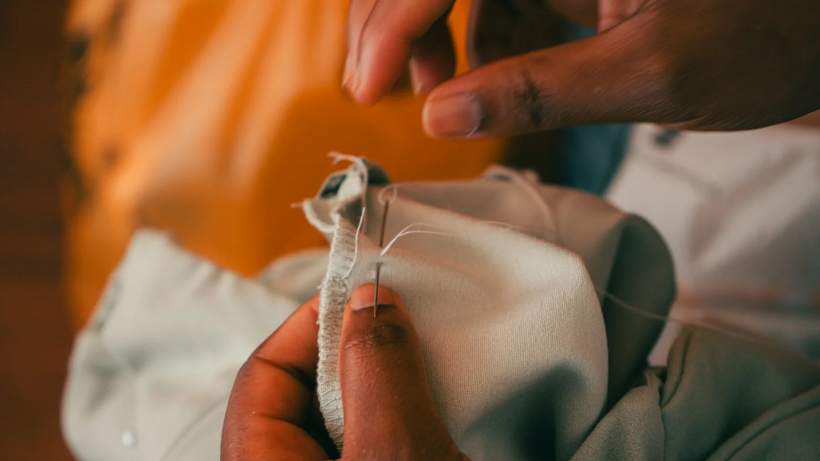 Hands working on light fabric with a needle and thread.