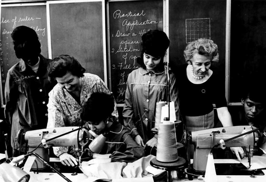 A historical black-and-white photograph of people working at a sewing class.