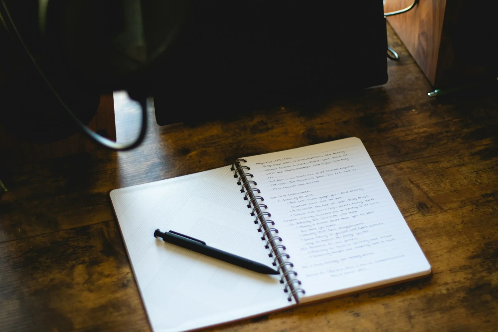 An open lined notebook and pen on a wooden writing table.