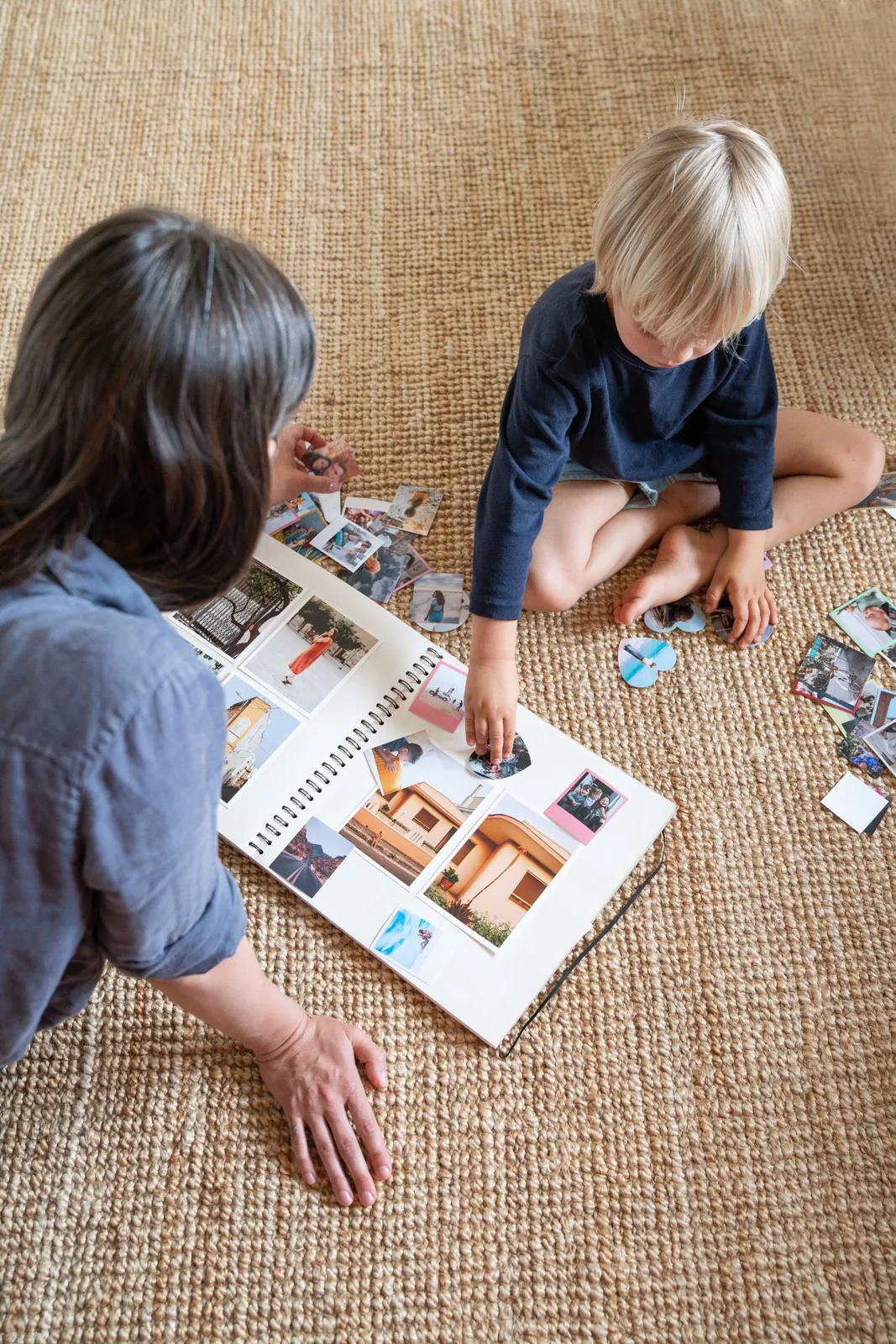A woman and child arranging photographs in a scrapbook on the floor.