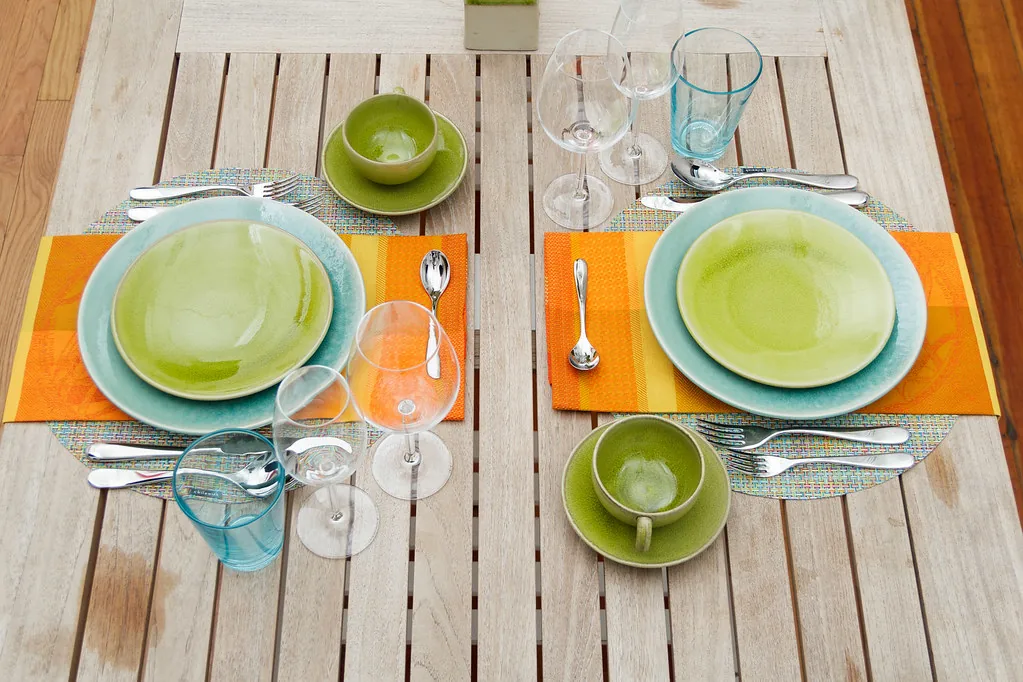 Two green place settings and glassware on a wooden dining table.