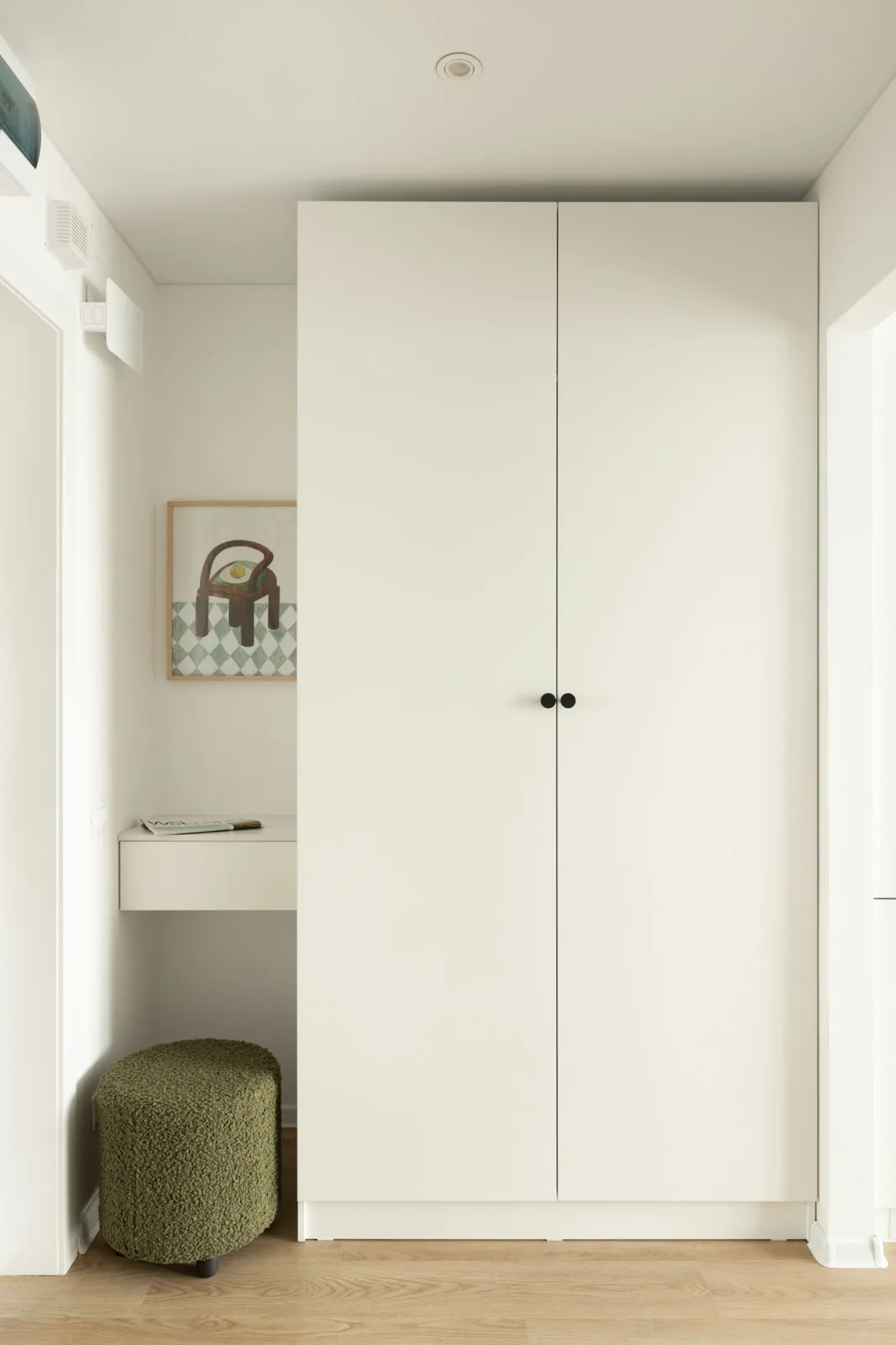 An apartment entrance with a white cupboard and green stool.